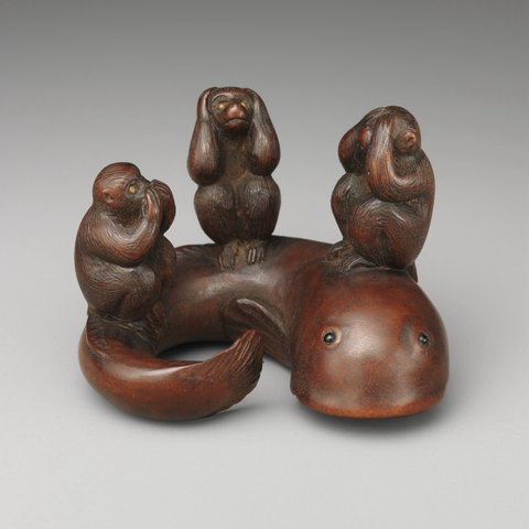 official museum photo of the object, front profile on gradient grey background finely carved wooden netsuke in the form of the “three wise monkeys” in a row on the back of a large eel-like fish