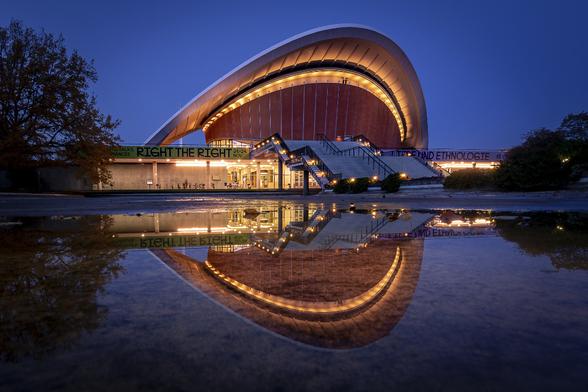 'Haus der Kulturen der Welt' building (Hiugh Stubbins architect) in Berlin, illuminated with golden light and reflected in water at blue hour.