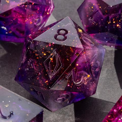 A dark pink D20 with of blue and champagne and bronze specks surrounded by parts of other dice.