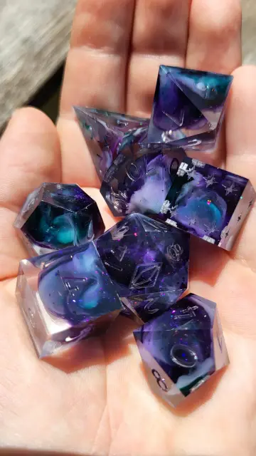 A dice set with teal and purple swirls in the palm of a hand