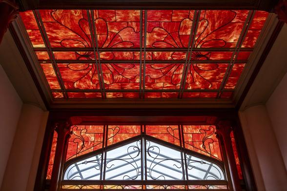 Low angle view on the Art nouveau stainglass ceiling and window at Hotel Winssinger in Brussels, adorned by big red flowers.
Victor Horta is the architect of this mansion which was recently renovated.