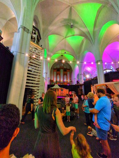 Inside the church, with neon green and purple lights hitting the ceiling. There's many people waiting for a tour!