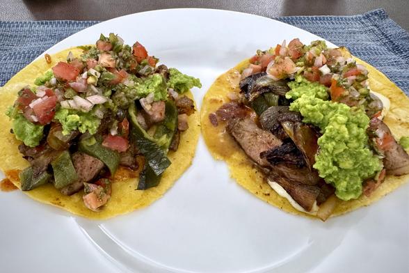 Two carne asada tacos served on a large white plate.