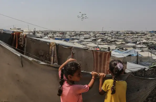 Children watch as parachutes drop symbolic aid over Rafah.