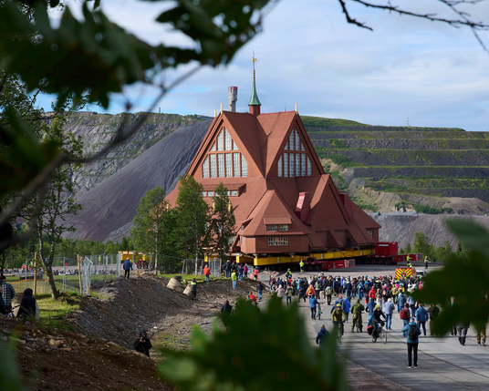From the article, a large red church building is placed on house-moving dollies, ready to be moved. A crowd stands outside. Mining artifacts are seen in the background.

he church, inaugurated in 1912, is known for its architecture that resembles a lávvu (a Sámi hut). Photograph: Malin Haarala/AP