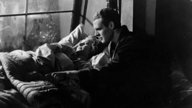 an image from the movie of a woman sleeping next to the window and a man next to her, he is awake, wearing a robe