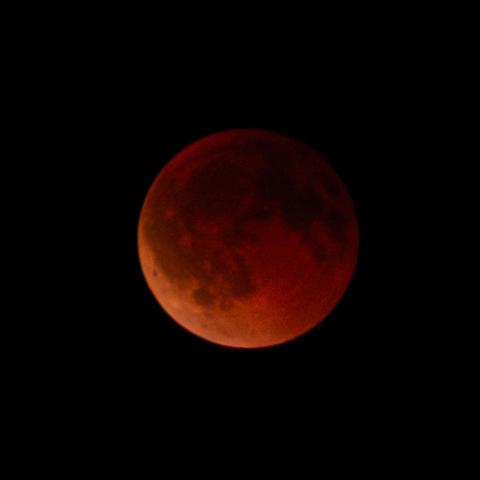 Blood moon during total lunar eclipse, the moon glowing deep red against a dark night sky.