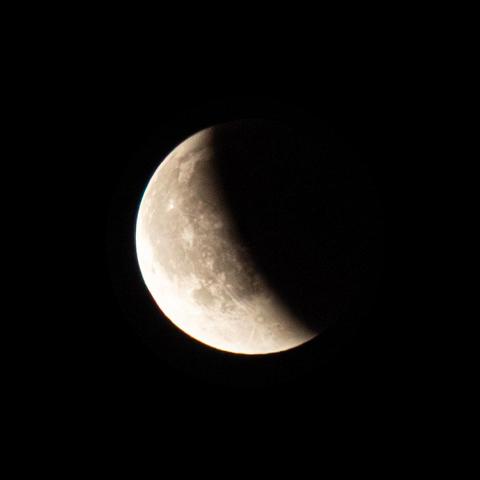 Moon in the late phase of the eclipse with almost all left half in bright light and the rest dark.