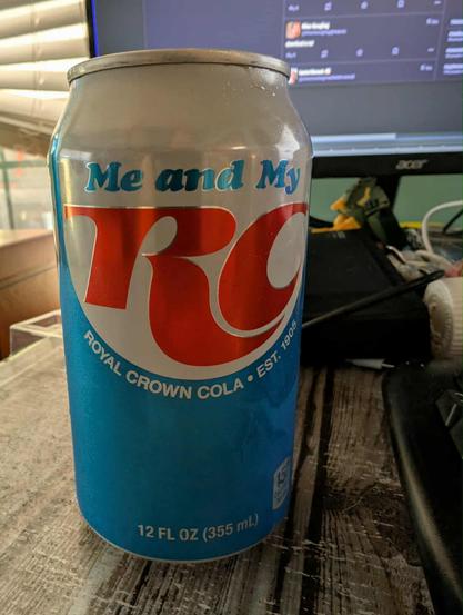 An ice cold can of RC cola sitting on a desk.  Can is red, white, and blue and is a retro aesthetic design meant to reference back to RC's 60s and 70s iconography