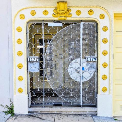 A decorative metal gate with a large, fan-shaped design, set in a white-and-yellow-trimmed archway. The archway is decorated with a row of small, yellow medallions.