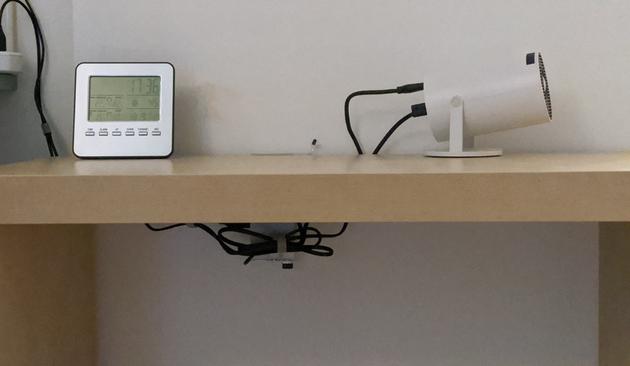 Projector sitting on a shelf, hidden below the shelf is a bunch of wires but all that's visible from above is a little LED