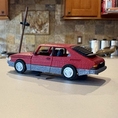 A red 3D-printed 1:64-scale 1990 Saab 900 SPG three-door hatchback, seen from a rear-3/4 angle.