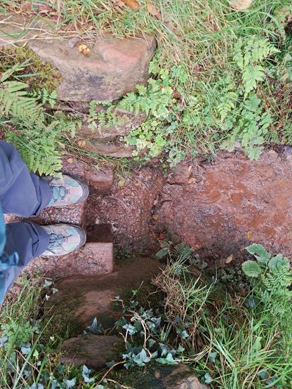Looking down at my legs in a tiny cut in the stone that intersects the muddy path.