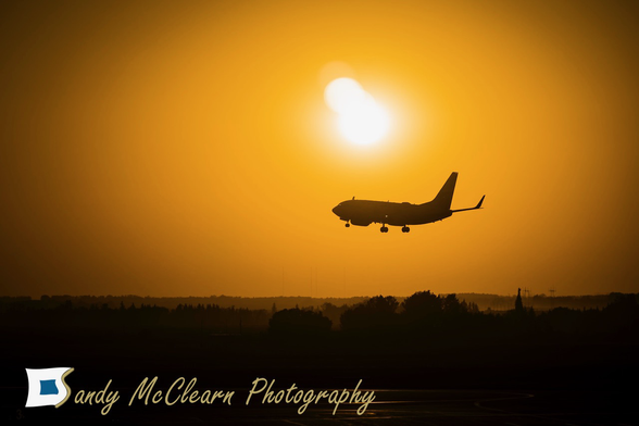 Airliner with landing gear down in silhouette on landing approach with orange sky and sun behind.