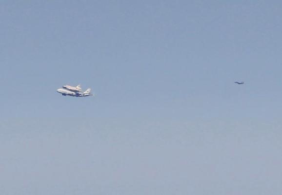 The space shuttle Endeavor wides atop its 747 carrier plane, with a chase plane behind it.