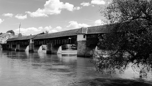 Schwarzweißfoto einer historischen gedeckten Holzbrücke auf steinernen Brückenpfeilern