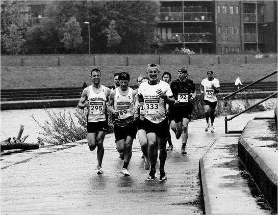 Runners, alongside a river. It is raining.