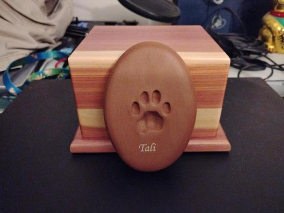 Image of an oval piece of clay with a cat's paw engraved into it with the name Tali below the paw print. Behind the clay paw print is the box where Tali's ashes are housed.