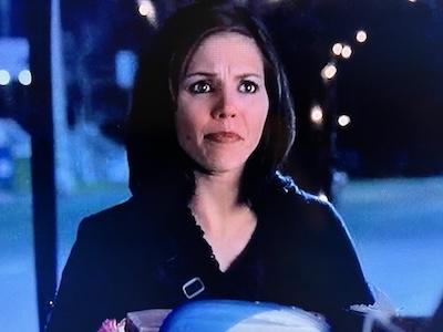 Cordelia Chase (Charisma Carpenter) looking distraught. She has white skin, reddish lipstick, hazel eyes, dark hair and is wearing dark clothing. There is a purse belt buckle visible on her right side. She is holding a random assortment of items, mostly office stuff. The setting is on the sidewalk near a street by the Hyperion Hotel. From Angel Season 2, Episode 11.