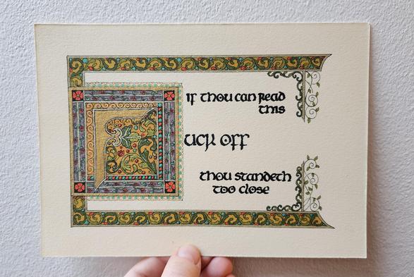 'If thou can read this, fuck off, thou standeth too close' calligraphed in black ink insular script. The 'fuck off' part is bigger and with a big ornamental F in gold in its own decorated box. There's a border of swirling leaves across the top and bottom, and bars with vines hanging down and up on the right, framing the text.