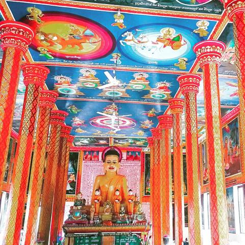 Photo shows a very colourful inside of a Buddhist Pagoda at Lolei in Roluos Group, Siem Reap. Strong red, yellow, orange and gold colours illustrates the pillars, walls and the central altar with a Buddha sculpture. The roof is painted with blue colours with motives collected from stories of the Buddhas life and the supporting figures. Cambodia is as safe, comfortable and kind as ever. Angkor and Siem Reap welcomes visitors. Enjoy your visit to the Kingdom of Wonder.
