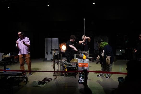 Heather stretches her blue spikey "fruit" bubble while Juom torches the neckline with the fluffy torch and Abbey is ready with face shield and gloves. I have donned the brittany spears mic and am gesturing with my hands as I explain what I am about to do to the public