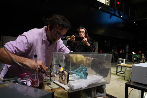 An action shot of me sealing the glass fruit inside of its protective acrylic box onto the manifold. Co director of the glass studio, Julia is behind me with the cell phone shot