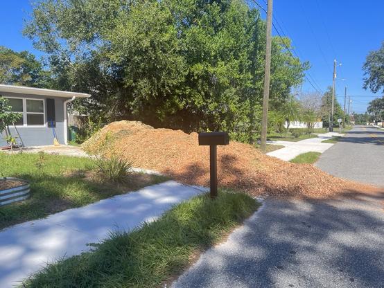 A huge pile of fresh brown mulch fills a suburban driveway and spills out into the street.