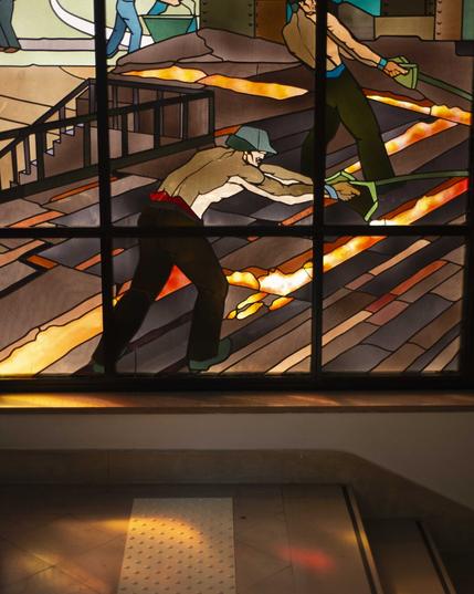 Vitrail représentant un ouvrier en casquette travaillant par dessus des coulées de métal en fusion Vitrail représentant un ouvrier en casquette travaillant par dessus des coulées de métal en fusion