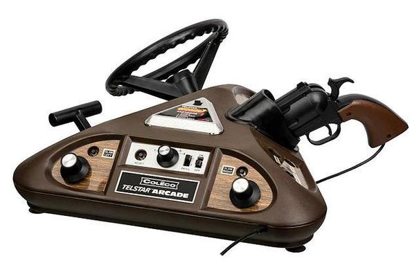 A brown triangular prism. The top side is used to for the triangular top-loading cartridges (this cartridge has Road Race, Tennis, and Quick Draw). The facing side is the pinball interface, with two paddles, a rotary switch, 'Slam Left', 'Slam Right', a skill selector, a power switch, and a reset button. The far side is a racing interface, with steering wheel and gear selector. The right side is shooting game interface, with a realistic looking sidearm and three buttons in holes. The interface panels alternate woodgrain and faux metal.