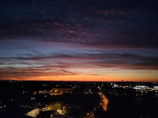 levé de soleil pastel, avec du bleu et du orange, plus les nuages qui forment un pattern doux, et la ville sombre aux petites lumière orange et jaune