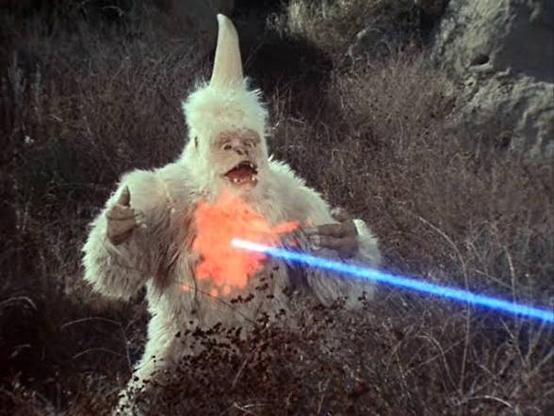 An alien that looks like a fierce albino gorilla with a large single horn coming out of its head being hit with phaser fire