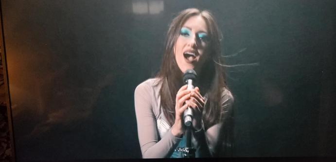 Diana Leah facing camera. Her eyes are ½ closed showing beautiful deep blue eye shadow. She had both hands on the mic in a stand. Low key background