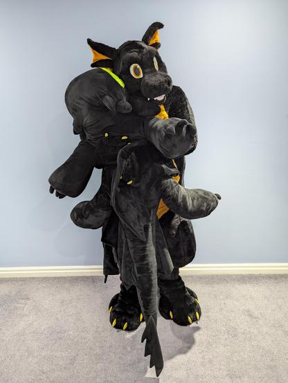 Black and copper dragon fursuit clutching an oversized plushie toothless
