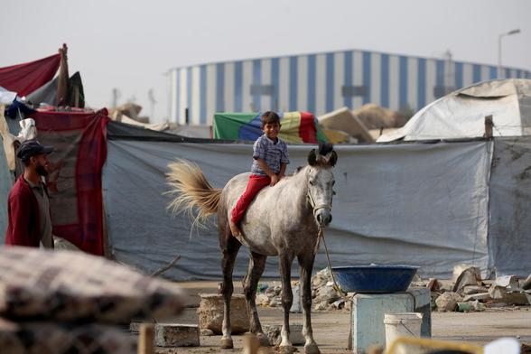 A Palestinian boy sits on a horse near a makeshift shelter in the Nuseirat refugee camp.