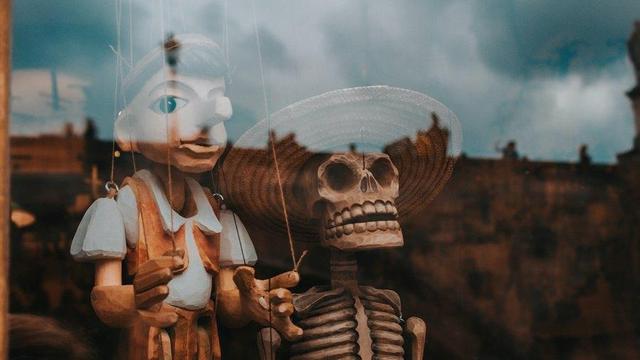 Photo of marionettes behind a glass window. One is Pinocchio, with a long nose. The other is a skeleton.
