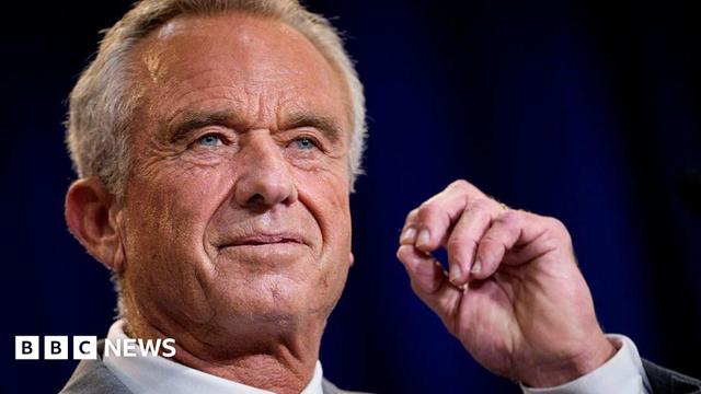 Close-up of the face of Robert F Kennedy Jr, who stares into the middle-distance with a curled hand close to his face 