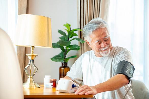 middle aged Asian man checking his blood pressure with a monitor at home