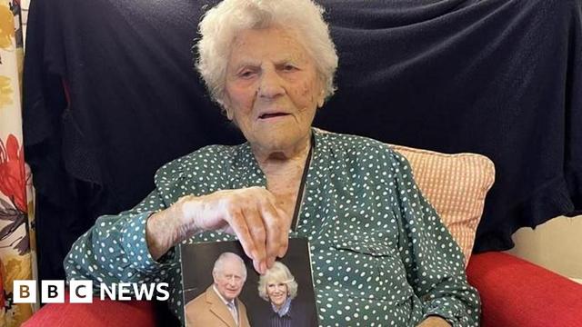 Ethel Caterham sat holding a card with a picture of the King and Queen on the cover.