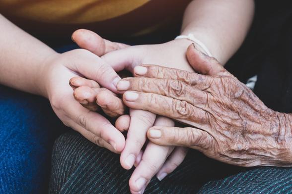 A close-up of hands of an older person and a child intertwined