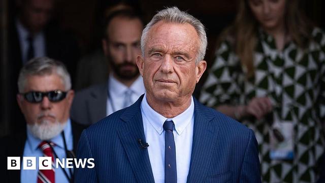 Robert F Kennedy Jr wearing a blue pin-striped suit with a think blue tie, with a blurred background