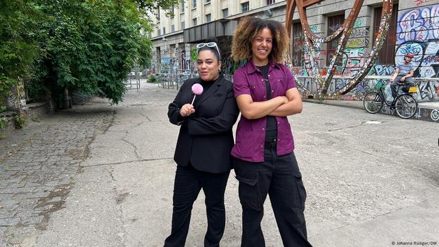 The Washington Post's Carmella Boykin and DW's Berlin Fresh content creator Briana Ekanem smile in front a a building covered with graffiti, the Berghain club.