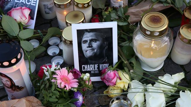 A black-and-white photo of Charlie Kirk, with his name written across it, is surrounded by candles and flowers.