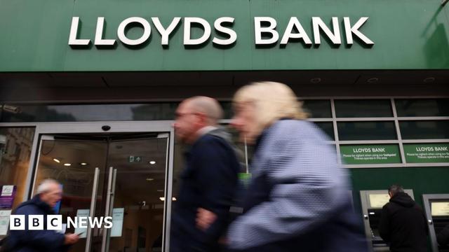 A shot of the front of a Lloyds Bank - it's branded name is in white lettering above the bank on its distinctive green background - in the foreground are a number of people walking and are out of focus, which draws focus to the bank's name - a person can also be seen taking money out of a cash machine A shot of the front of a Lloyds Bank - it's branded name is in white lettering above the bank on its distinctive green background - in the foreground are a number of people walking and are out of focus, which draws focus to the bank's name - a person can also be seen taking money out of a cash machine